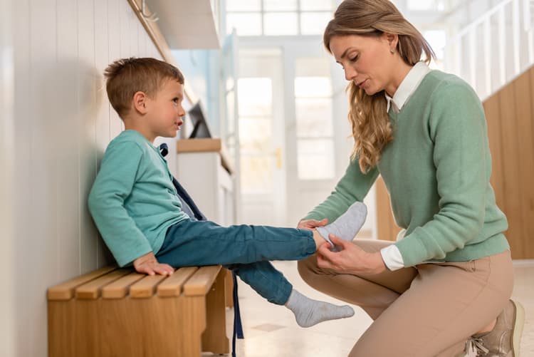 Kto może opiekować się dzieckiem w przedszkolu? Statutowe zasady powierzania opieki nad dziećmi. Na zdjęciu: nauczycielka pomaga dziecku założyć buty.